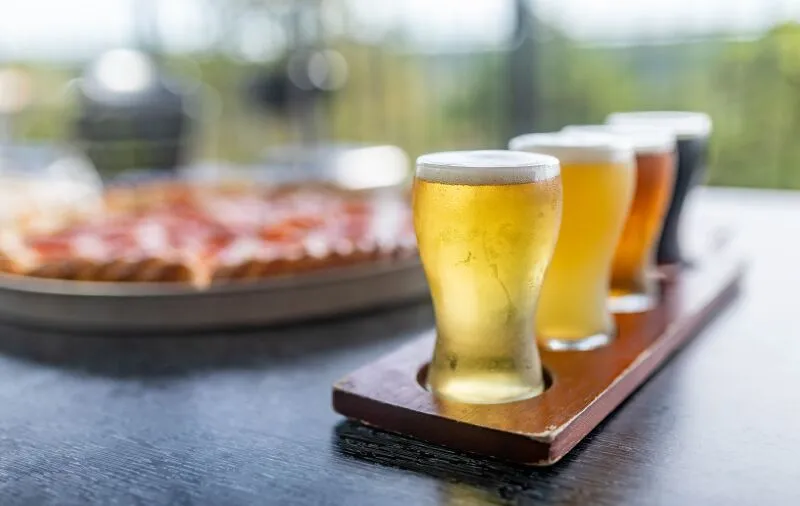 A flight of four beers and a pizza on a table.