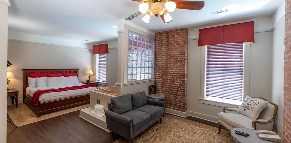 A wide-angle view of a hotel room with a bed, sofa, chair, and coffee table.