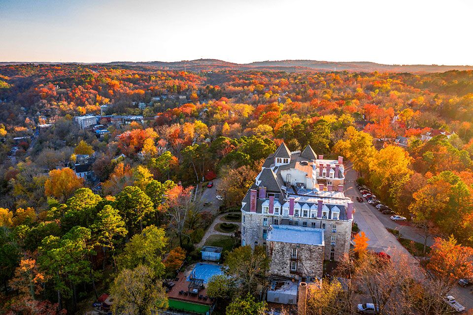 Aerial view of a large stone building with a slate roof, surrounded by trees with fall colors.