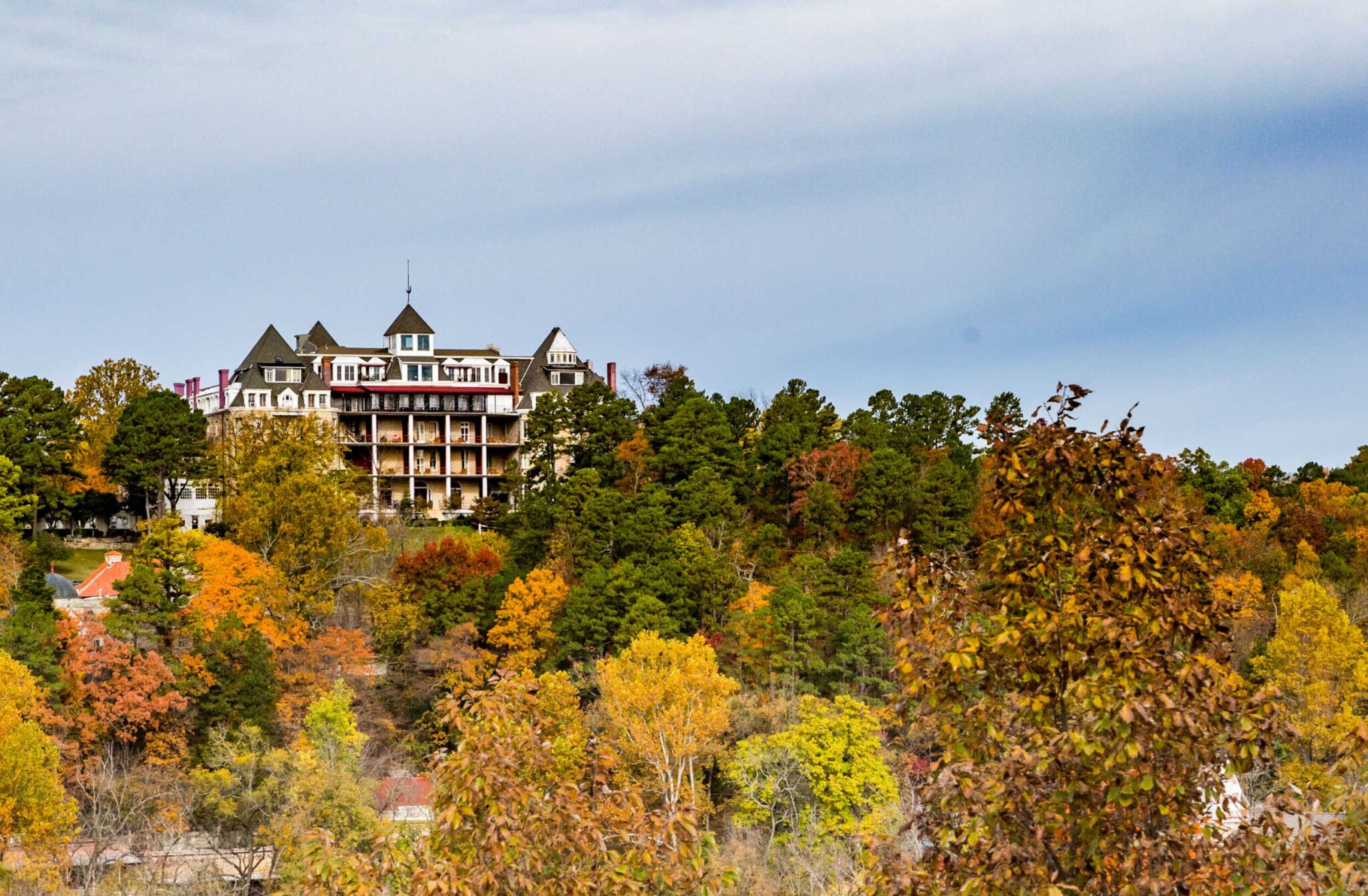 A large white building with a dark roof is surrounded by trees with changing leaves.