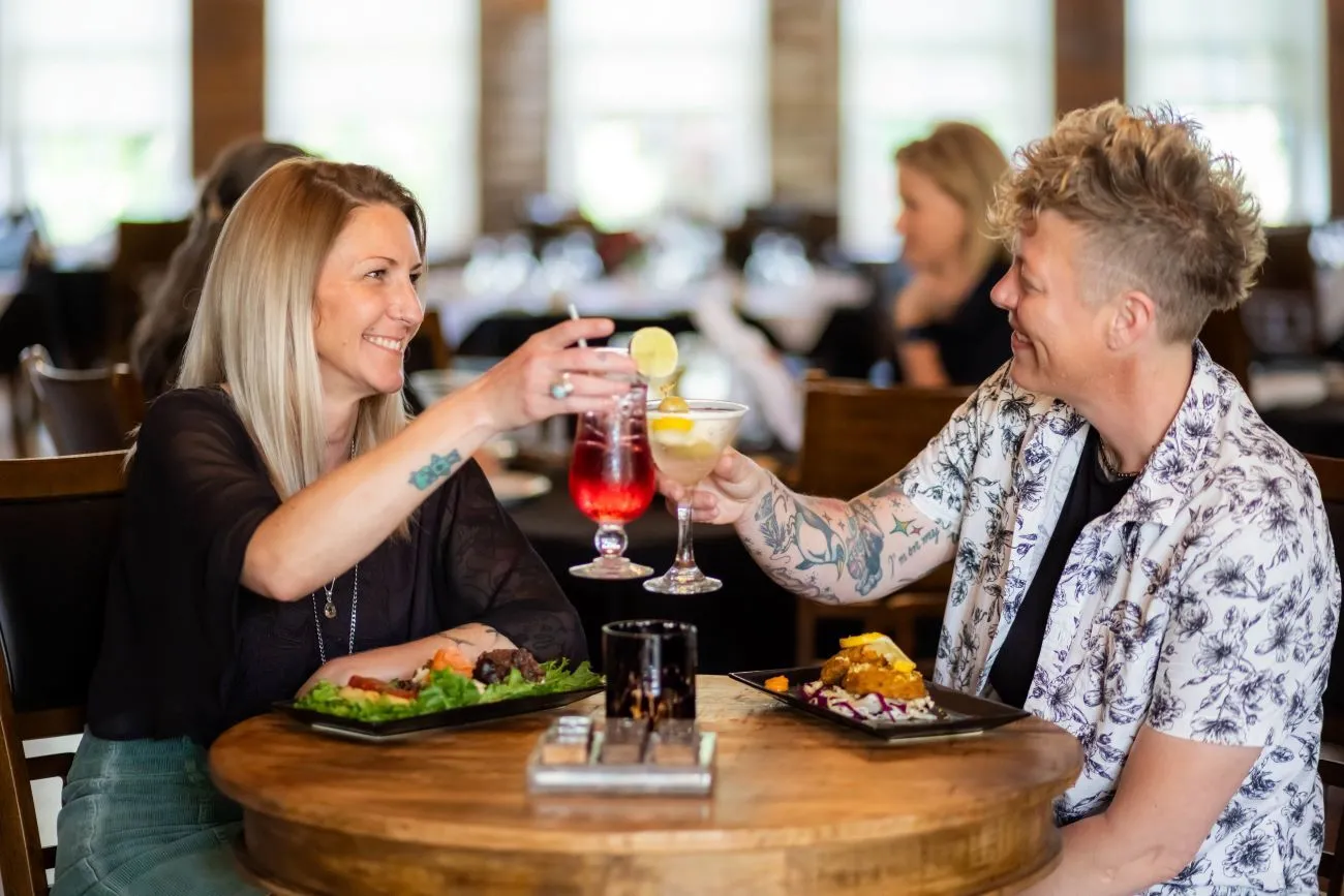 Two people sitting at a table with food and drinks