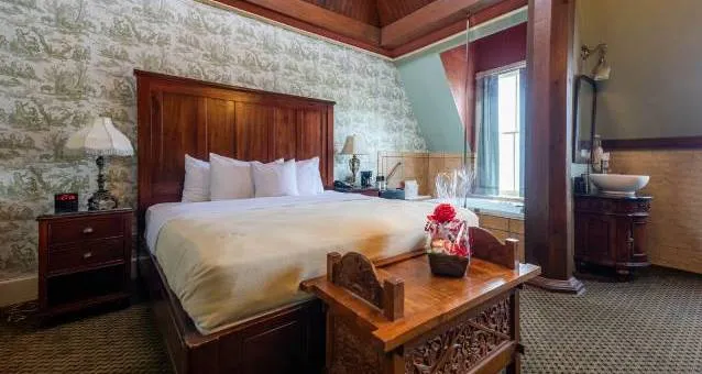 A wide view of a hotel room with a king-size bed, wooden furniture, and floral wallpaper.