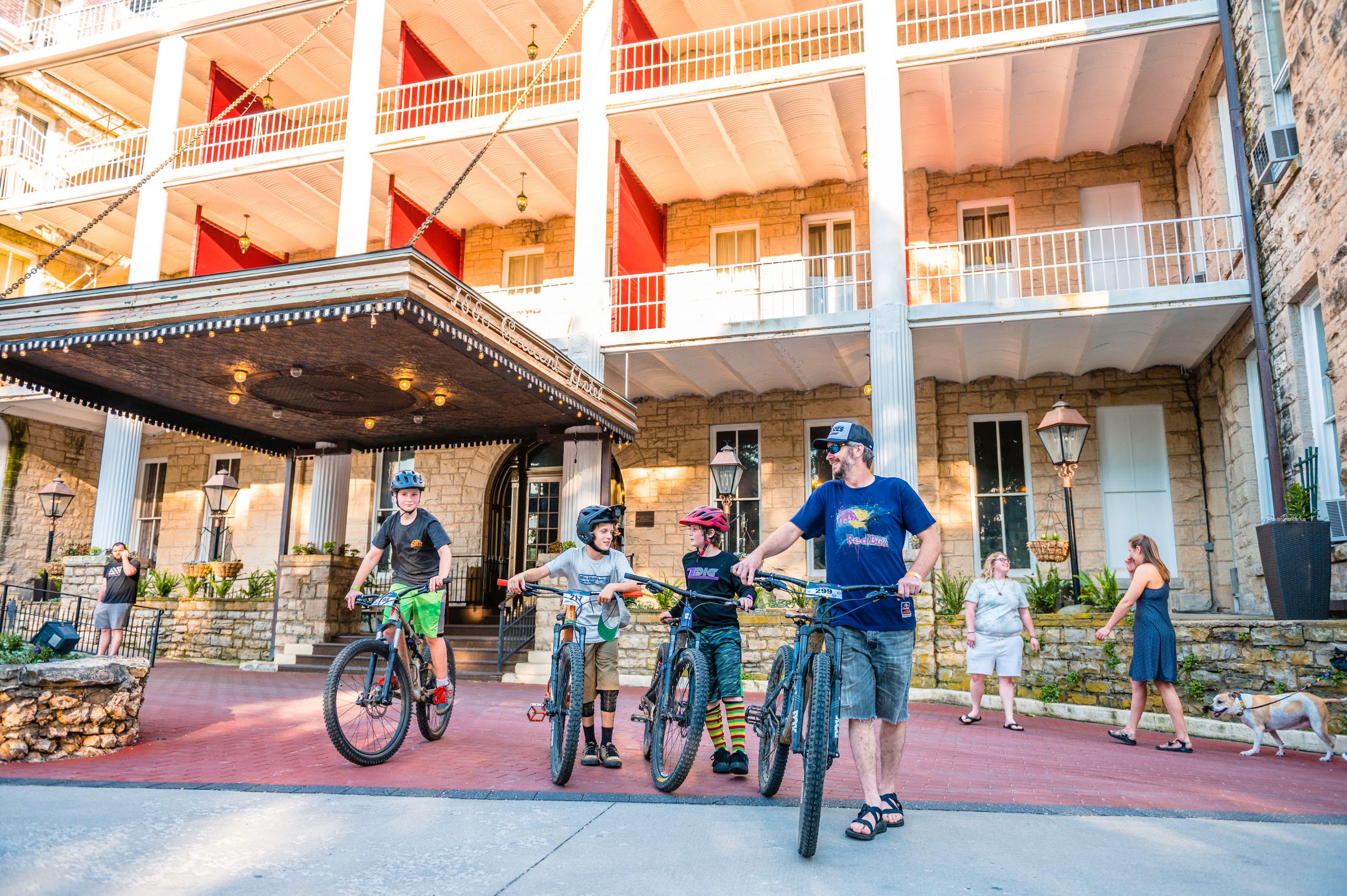 A family with bicycles in front of a stone building with balconies and red trim.